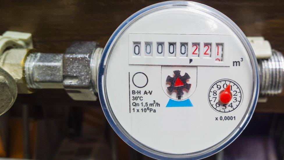 An analog water meter face showing a series of black and red numbers, with a rotating dial and other indicators, used to measure water consumption.