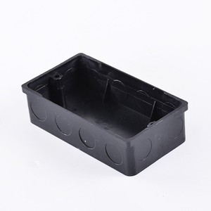 A black, rectangular electrical conduit box with multiple circular entry points on the sides and two screw holes on the top rim.