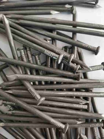 A close-up, top-down view of a large pile of grey, rustic-looking steel nails with ridged shanks and flat heads, jumbled together.