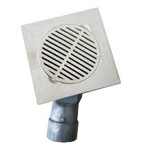 A white plastic single-way floor trap on a white background. This square-shaped drain has a round, slotted grate on top and a pipe extending from the bottom at an angle, designed to be installed in a floor to collect water and prevent bad odors from entering the room.