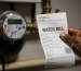 A high water bill being held, with a smart water meter in the background.