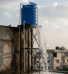 A large, elevated water storage tank on a rooftop visibly overflowing